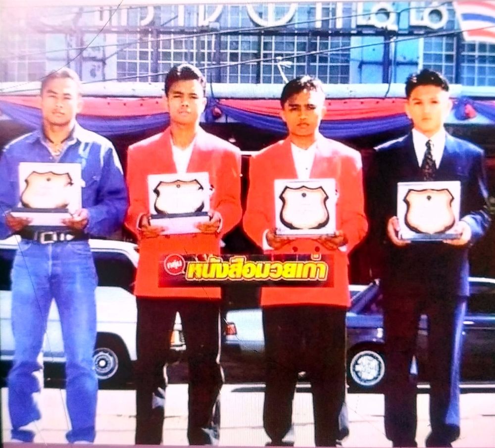 Four fighters holding award plaques outside a stadium in Thailand