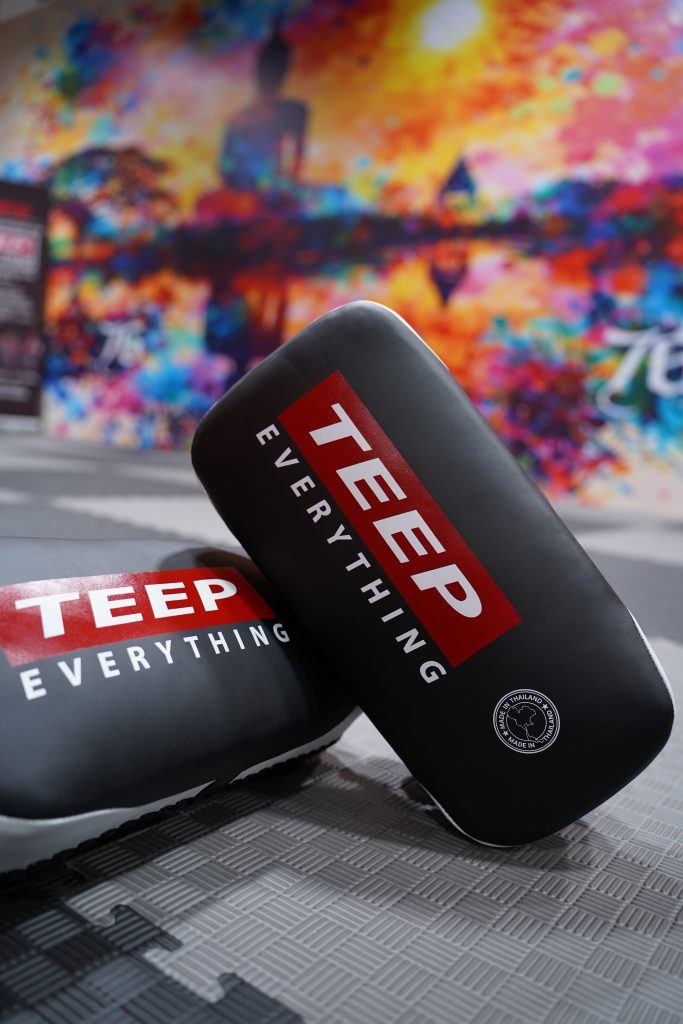 TEEP Everything branded Thai pads on the gym mats, with the Buddha mural behind